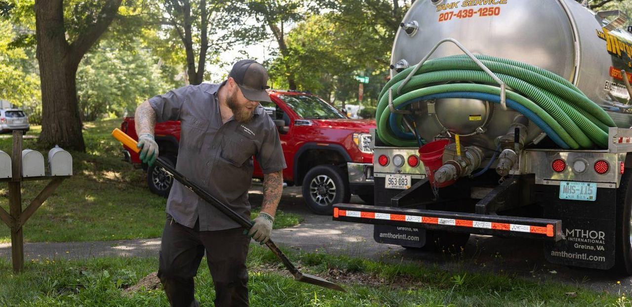A Morgridge crew working a septic pumping call at a house, hose run from the truck across the lawn.