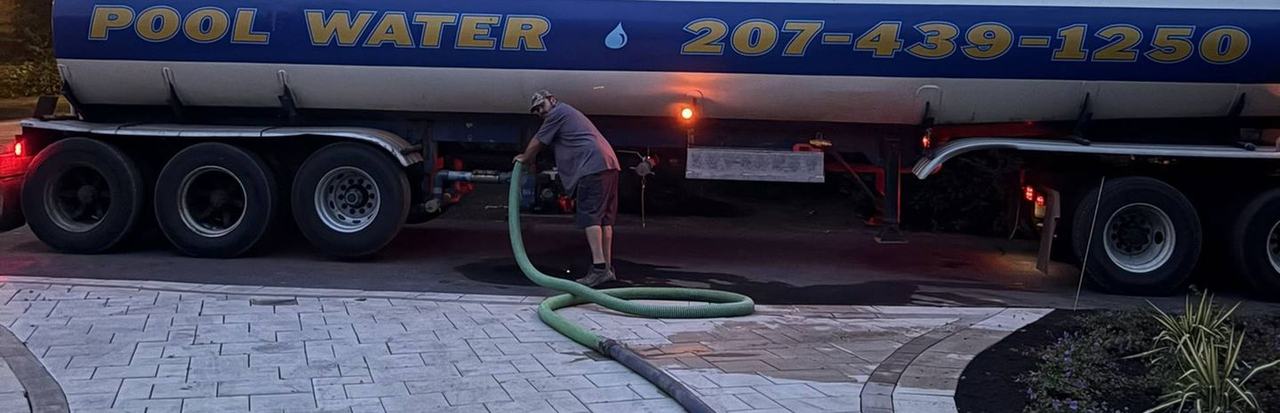 The dedicated clean-water tanker on a residential driveway with the delivery hose run out toward a backyard pool.