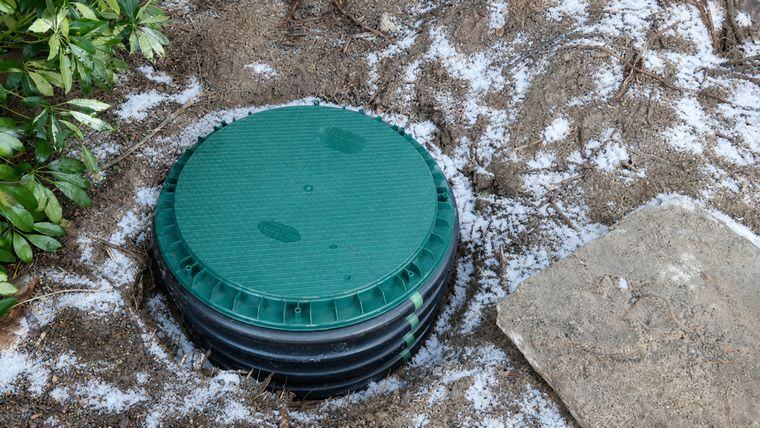 A green septic riser lid sitting flush at grade in the yard.